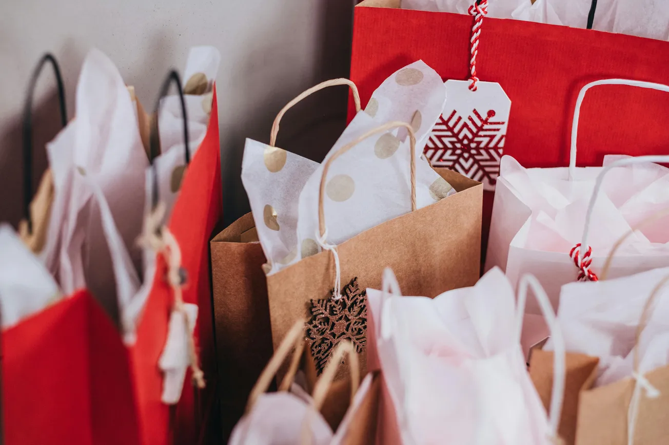 Close-up of festive gift bags with red and brown paper, filled with white tissue paper. A snowflake decoration adds a cheerful holiday touch.